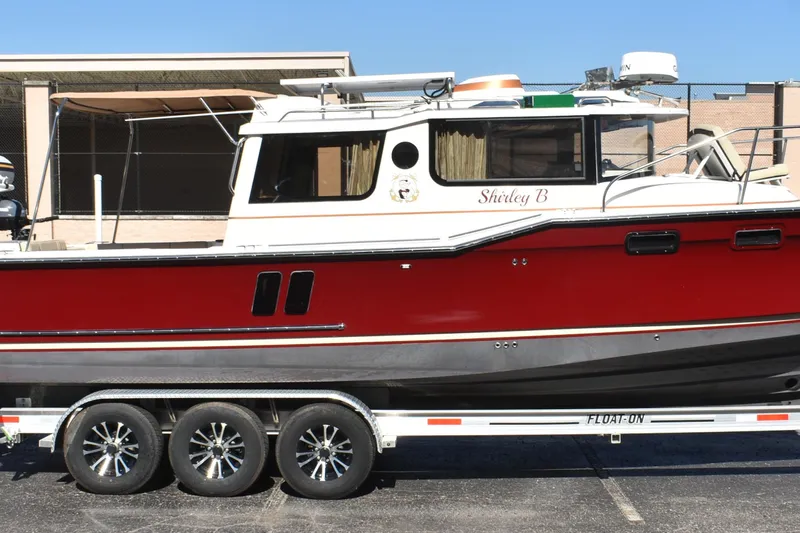 Slide: The Image of 2024 Ranger Tugs R-27 boat on trailer, red and white exterior, parked outdoors. - 5