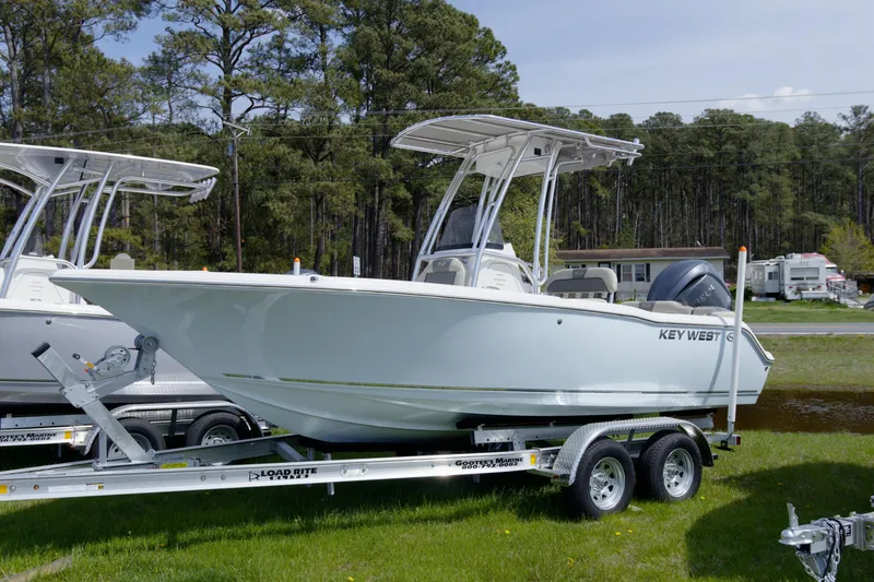 Slide: The Image of 2026 Key West 203 FS boat on trailer, parked on grass with trees in background. - 10