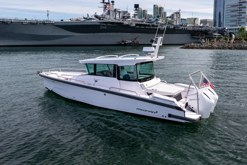 Slide: The Image of 2026 Axopar 29 XC Cross Cabin boat on water near a large ship and cityscape. - 14