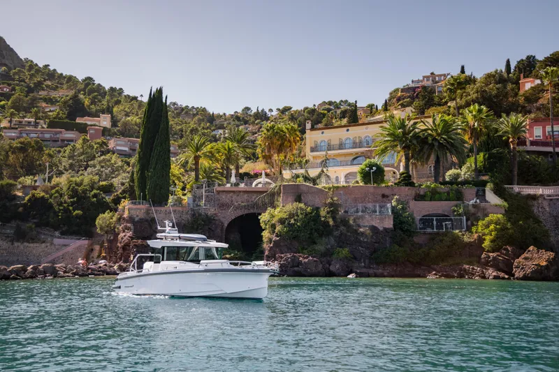 Slide: The Image of 2026 Axopar 29 XC boat cruising near scenic coastal villa with lush greenery. - 4