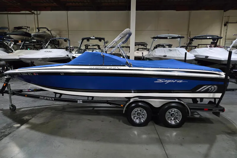 The Image of 2005 Supra Sunsport 22 V boat in showroom, blue cover, on trailer. - 1