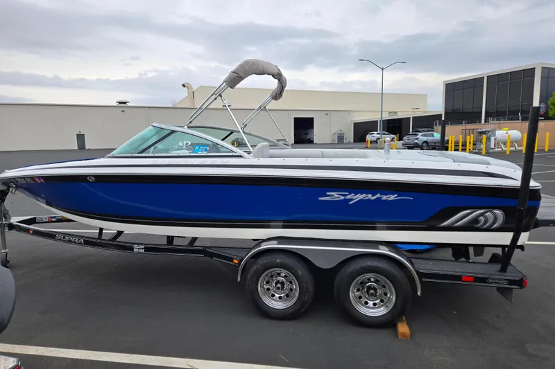 Slide: The Image of 2005 Supra Sunsport 22 V boat on trailer, blue and white design, parked outdoors. - 9