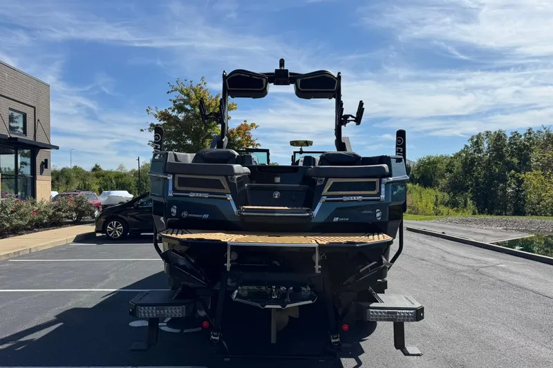 Slide: The Image of 2025 MasterCraft XStar 25 boat parked outdoors, rear view with clear sky background. - 5
