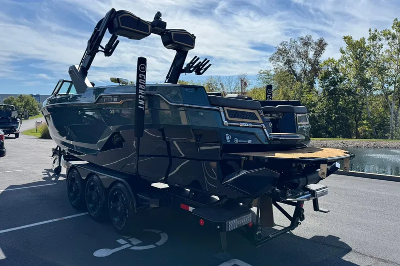 Slide: The Image of 2025 MasterCraft XStar 25 boat on trailer, parked near a scenic lake. - 6