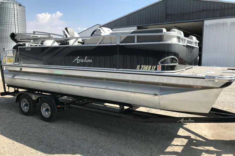 The Image of 2024 Avalon VENTURE FISH-N-CRUISE pontoon boat on trailer, parked near industrial buildings. - 3