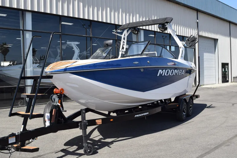 Slide: The Image of 2025 Moomba Craz boat on trailer, blue and white, parked outside a showroom. - 2