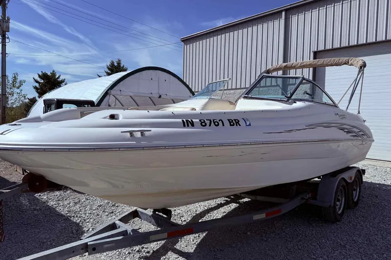 The Image of 2000 Sea Ray 210 Sundeck boat on trailer, parked outdoors near a metal building. - 0