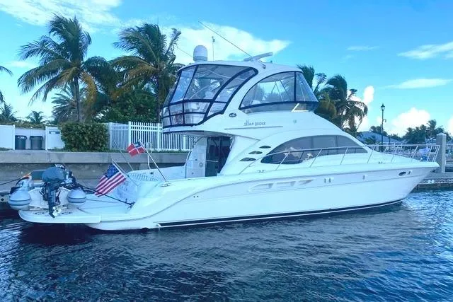 Slide: The Image of 2007 Sea Ray 52 Sedan Bridge yacht docked by palm trees, featuring sleek design and flags. - 3