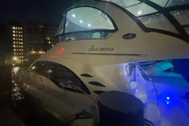 Slide: The Image of 2007 Sea Ray 52 Sedan Bridge yacht illuminated at night, docked with city lights in background. - 52
