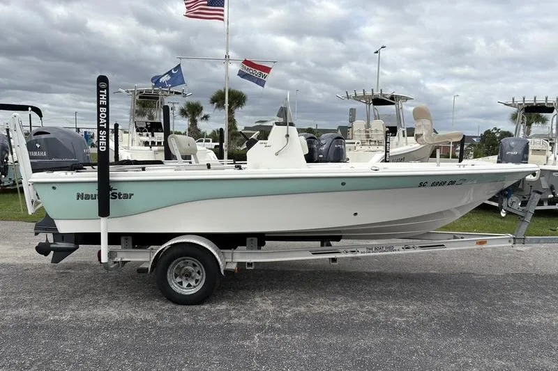Slide: The Image of 2015 NauticStar 1910 NauticBay boat on trailer, displayed outdoors with flags in background. - 7