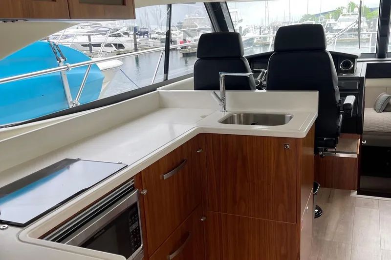 Slide: The Image of 2020 Riviera 4800 Sport Yacht interior with modern kitchen and helm, docked at marina. - 4
