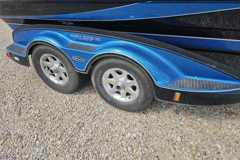 Slide: The Image of 2007 Triton 21 X-2 DEMO boat trailer with dual wheels on gravel surface. - 14