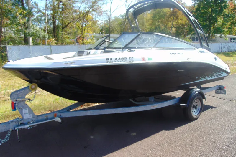 The Image of 2023 Yamaha Boats AR190 on trailer, parked outdoors, surrounded by trees and fencing. - 2