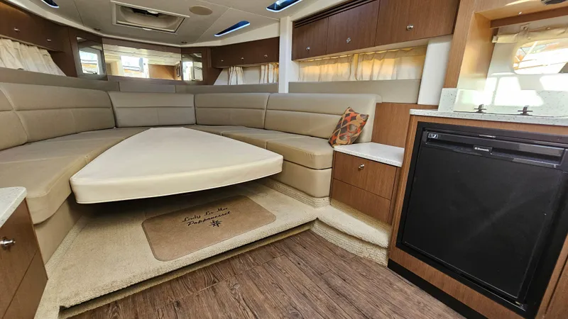Slide: The Image of 2014 Sea Ray 350 Sundancer interior with beige seating, wooden cabinetry, and compact kitchenette. - 19