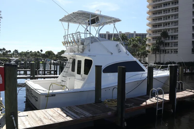 Slide: The Image of 2005 Luhrs 38 Convertible yacht docked at marina, surrounded by buildings and palm trees. - 62