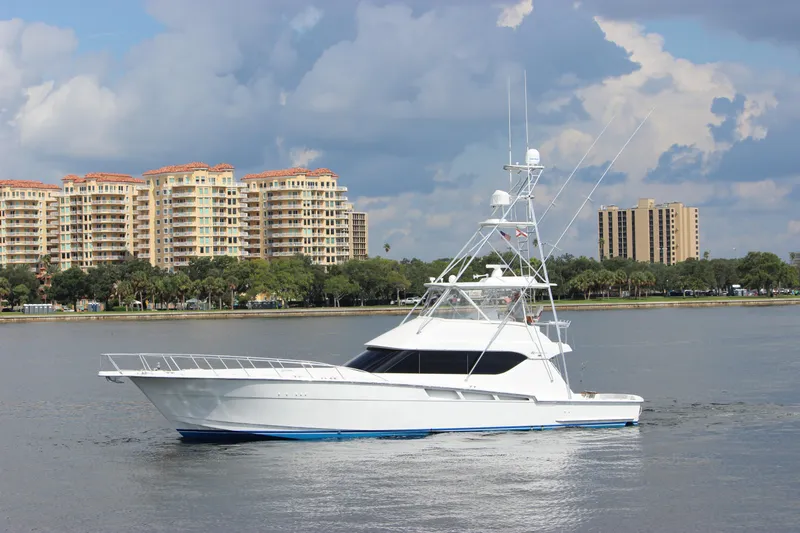 Slide: The Image of 2004 Hatteras 60 Convertible yacht cruising near waterfront buildings under cloudy sky. - 1