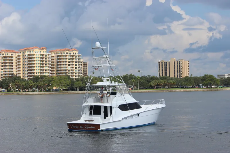 Slide: The Image of 2004 Hatteras 60 Convertible yacht cruising near waterfront buildings under cloudy sky. - 6