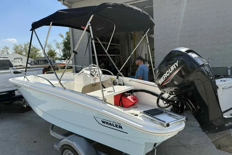 Slide: The Image of 2024 Boston Whaler 130 Super Sport boat with Mercury engine and canopy, parked outdoors. - 2