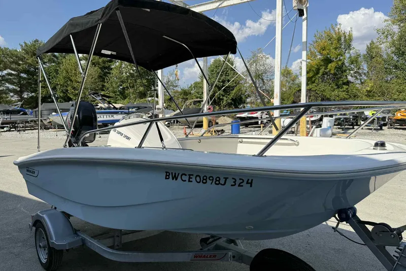 Slide: The Image of 2024 Boston Whaler 130 Super Sport boat with canopy on a trailer, parked outdoors. - 5