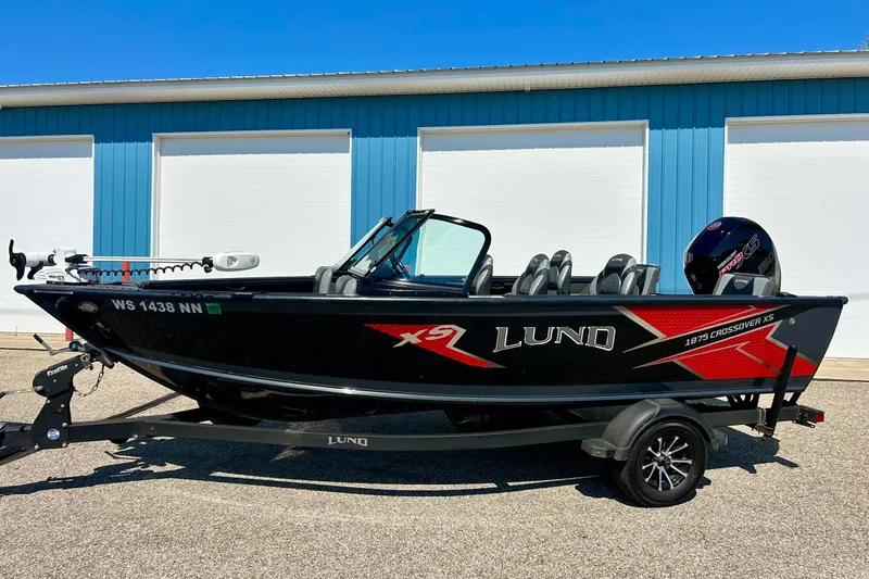 Slide: The Image of 2021 Lund 1875 Crossover XS boat with trailer, parked outside blue building. - 2