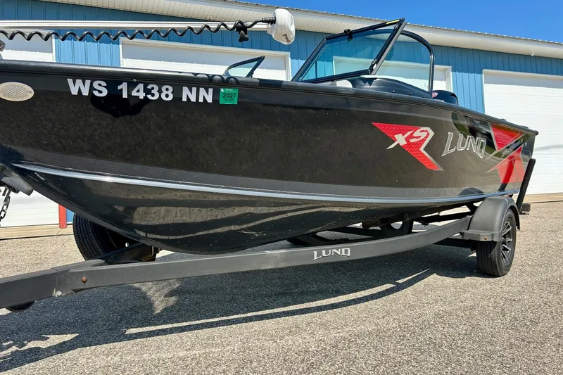 Slide: The Image of 2021 Lund 1875 Crossover XS boat on trailer, black with red accents, parked outdoors. - 60