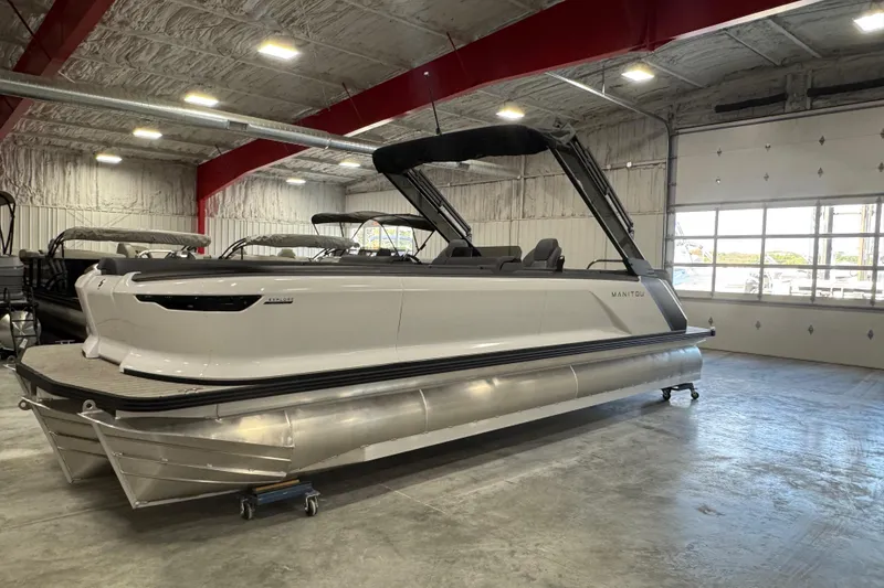Slide: The Image of 2025 Manitou 26 Explore pontoon boat in a showroom, featuring sleek design and modern amenities. - 2