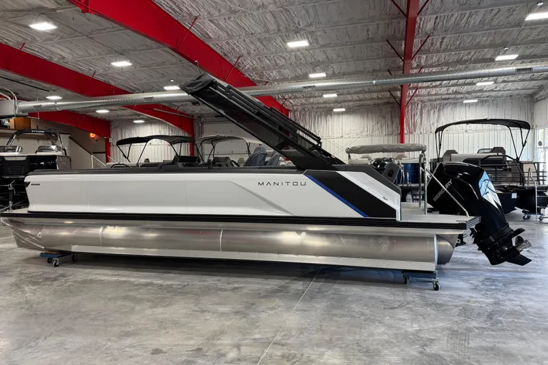 Slide: The Image of 2025 Manitou 26 Explore pontoon boat in a showroom with red beams. - 4