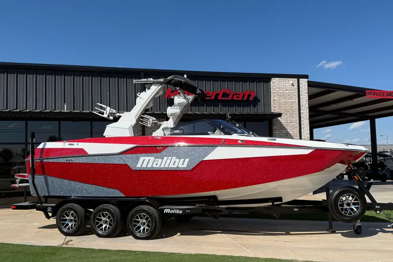 Slide: The Image of 2021 Malibu M240 boat in red and white, parked outside a dealership. - 0