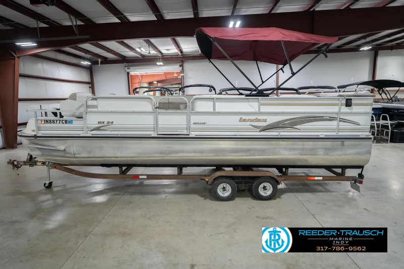 Slide: The Image of 1999 Landau DX24 pontoon boat with red canopy on trailer in indoor showroom. - 11