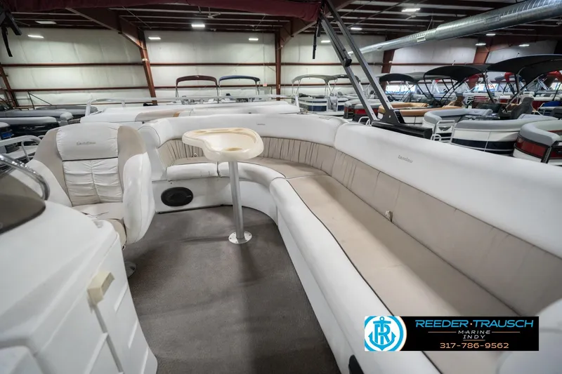 Slide: The Image of 1999 Landau DX24 pontoon boat interior with beige seating and small table in showroom. - 27