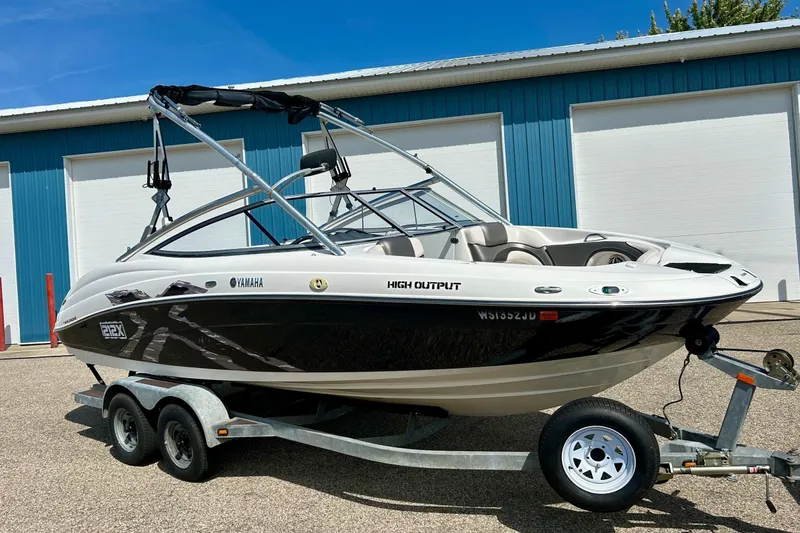 The Image of 2008 Yamaha 212X boat on trailer, parked near blue building, sunny day. - 1