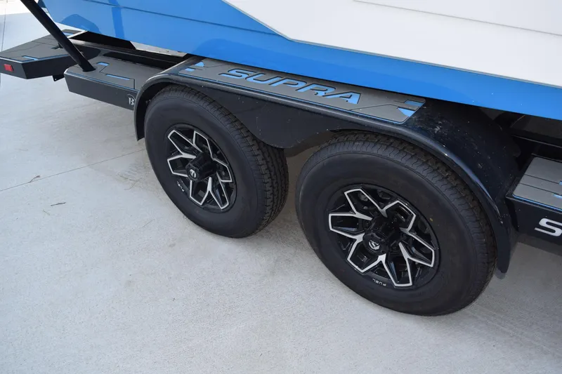 Slide: The Image of 2026 Supra SA boat in showroom, featuring sleek design and dual-axle trailer. - 13