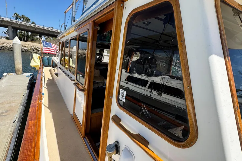 Slide: The Image of 1980 Californian Tri-Cabin Trawler docked, featuring wooden trim and American flag. - 25