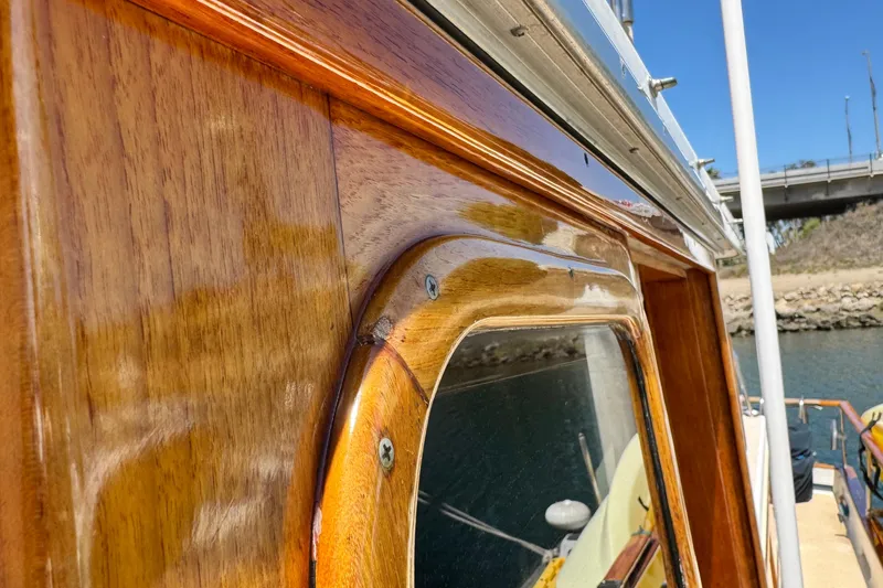 Slide: The Image of Close-up of 1980 Californian Tri-Cabin Trawler's polished wooden exterior by the water. - 26