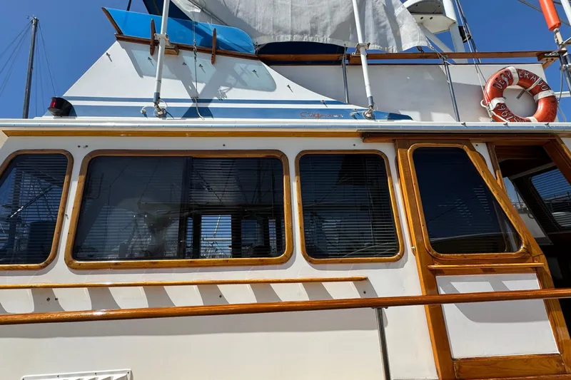 Slide: The Image of 1980 Californian Tri-Cabin Trawler with wooden trim and lifebuoy, under clear blue sky. - 4