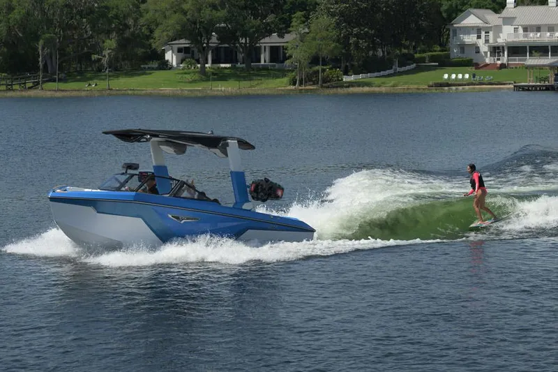 Slide: The Image of Manufacturer Provided Image: 2025 Nautique Super Air Nautique S23 towing a wakeboarder on a scenic lake. - 18