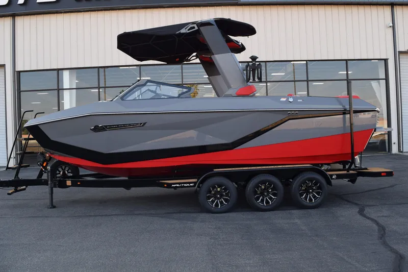 Slide: The Image of 2025 Nautique Super Air Nautique G23 boat, gray and red, on a trailer outside a building. - 1