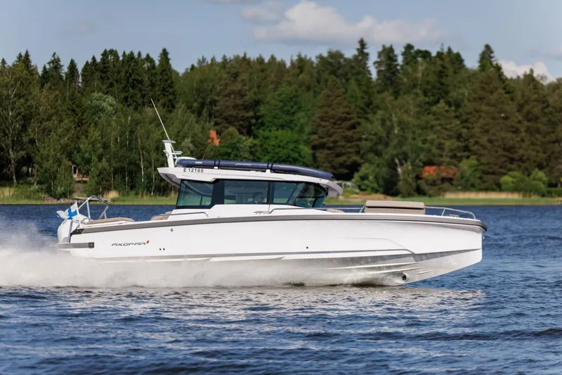 The Image of 2026 Axopar 29 XC Cross Cabin boat cruising on a scenic lake with forested background. - 0