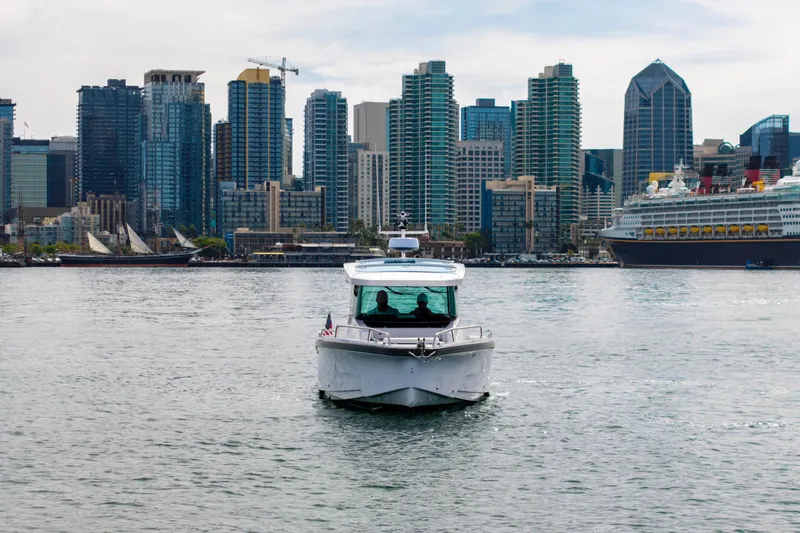 Slide: The Image of 2026 Axopar 29 XC Cross Cabin boat cruising in urban harbor with city skyline backdrop. - 2