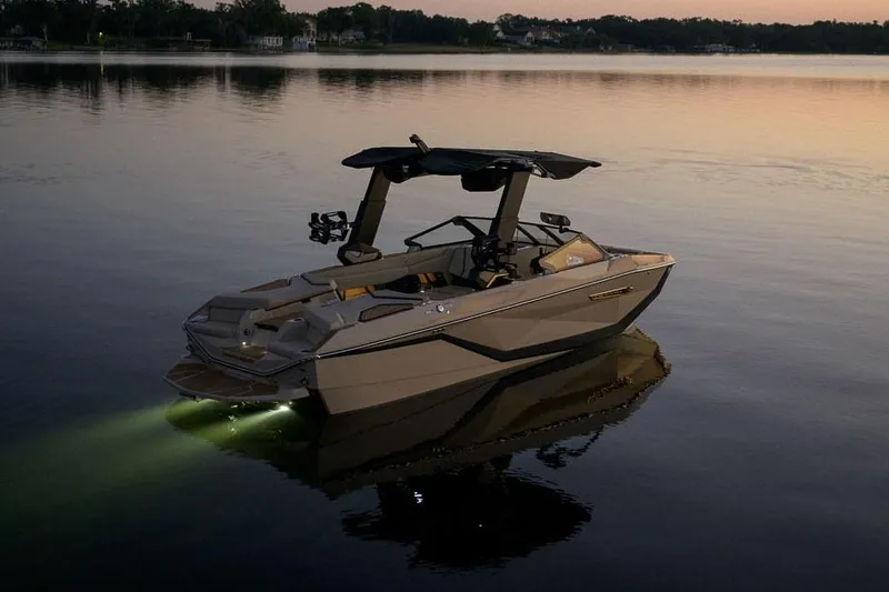 Slide: The Image of Manufacturer Provided Image: 2026 Nautique Super Air Nautique G23 boat on calm water at sunset with lights on. - 15