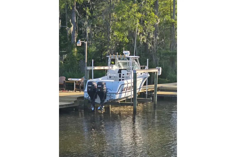 Slide: The Image of 1993 Robalo 2440 boat docked by a wooded shoreline with dual outboard motors. - 30