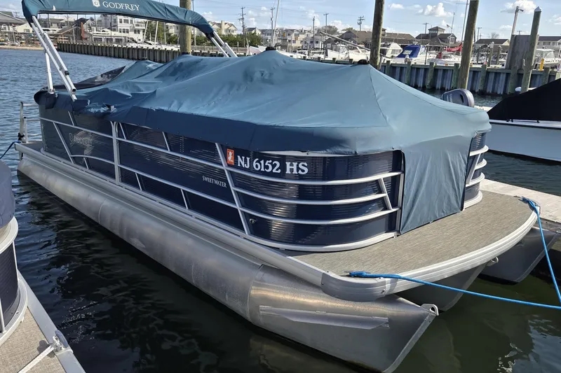 Slide: The Image of 2023 Godfrey Sweetwater 2286 SBX pontoon boat interior with seating and helm, docked by the water. - 4
