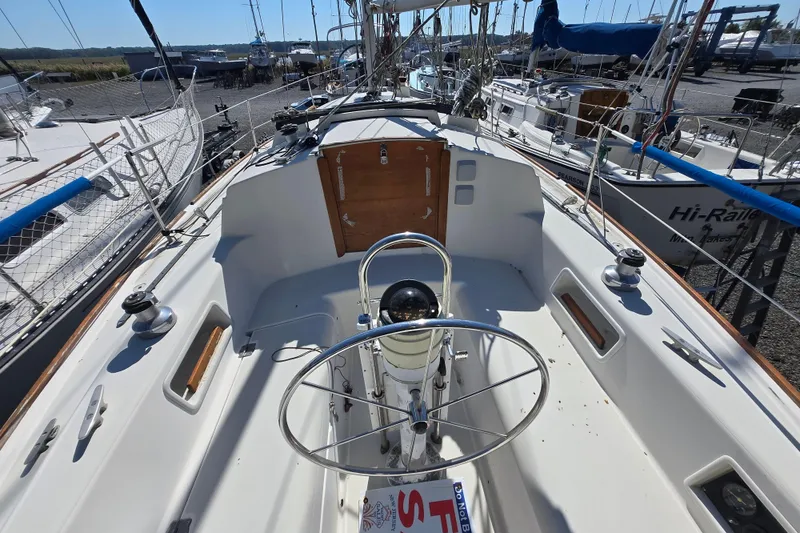 Slide: The Image of 1986 Pearson 303 Sloop sailboat cockpit with steering wheel, docked among other boats. - 31