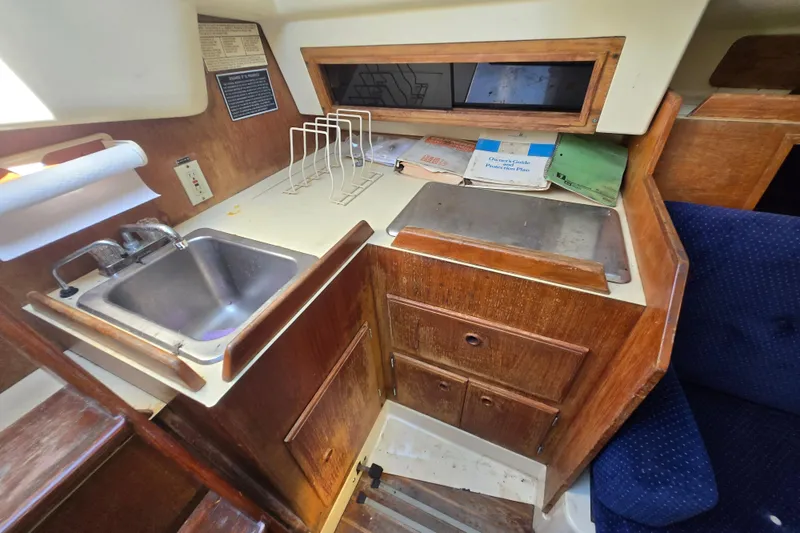Slide: The Image of 1986 Pearson 303 Sloop interior galley with sink, storage, and manuals on counter. - 14