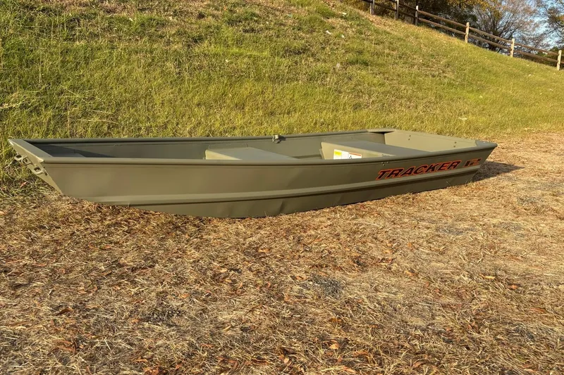 Slide: The Image of 2026 Tracker Grizzly 12 Jon boat on grassy terrain, side view. - 2