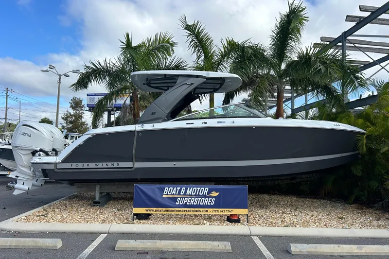 The Image of 2026 Four Winns H9 OB boat displayed at dealership with palm trees in background. - 1