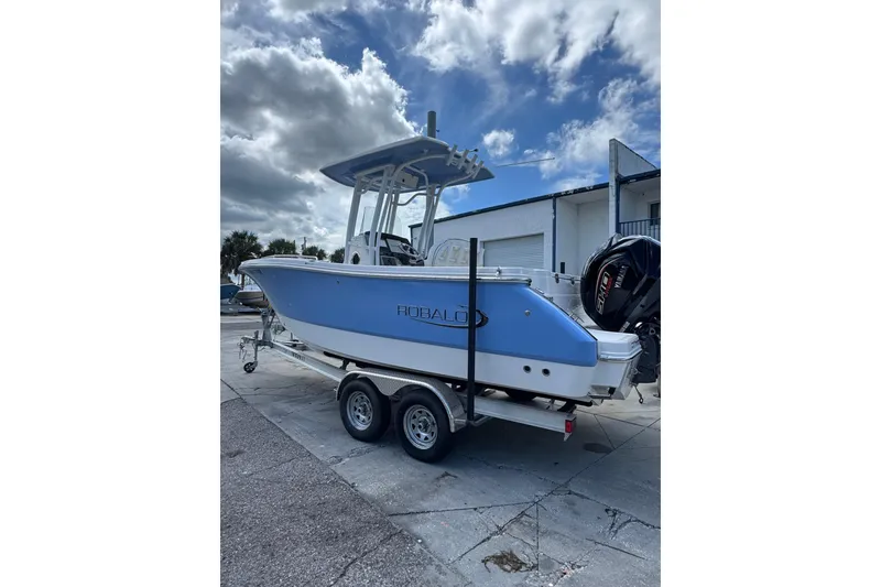 The Image of 2024 Robalo R230 Center Console boat on trailer, blue hull, outdoor setting. - 0