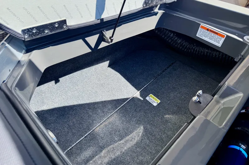 Slide: The Image of Open storage compartment in 2020 MasterCraft XStar boat, featuring carpeted interior and caution label. - 37