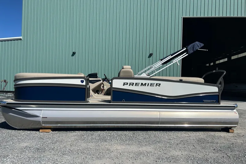 Slide: The Image of 2026 Premier 230 Solaris RF pontoon boat parked outside a green building. - 2
