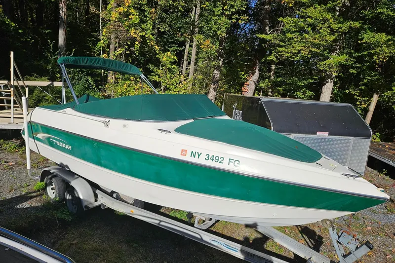 The Image of 2001 Stingray 240 LS boat on trailer, green and white, parked in wooded area. - 0